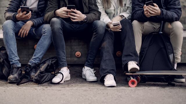 Teenage boys and girl using smart phone while sitting at park SMALL